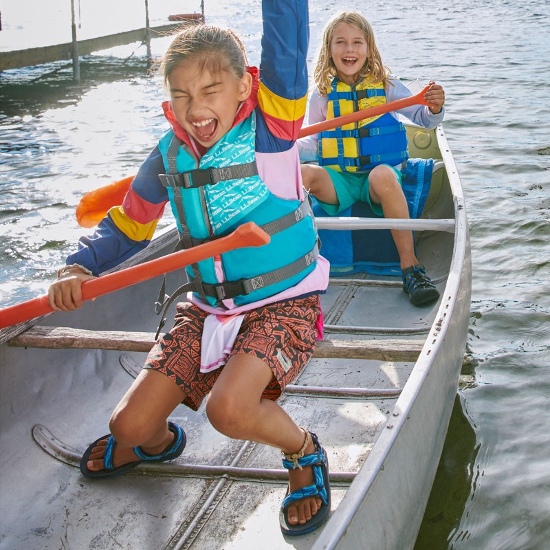 2 kids wearing PFDs paddling a canoe.