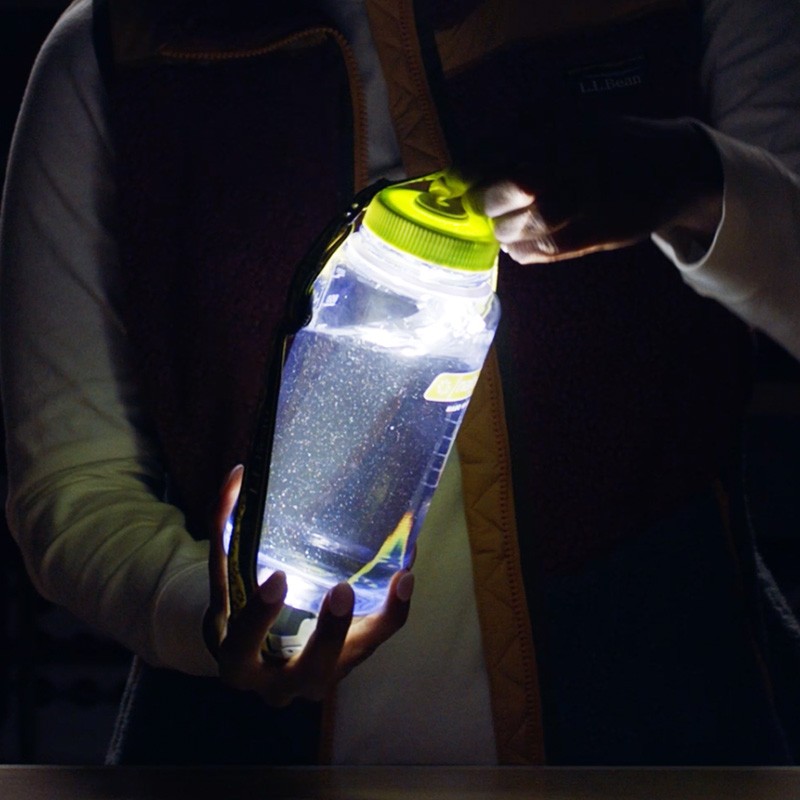 A full water bottle with a headlamp strapped to it glowing with light in the dark.