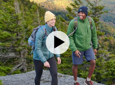 2 people hiking, a play video icon in the center.