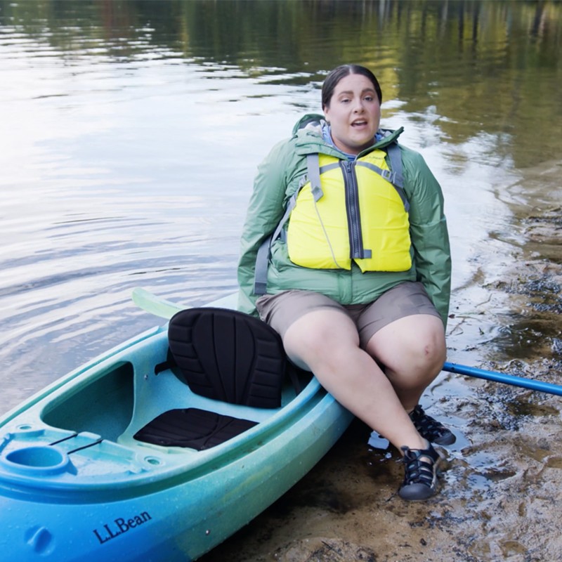 MacKenzie sitting just behind the cockpit of a kayak on the beach.