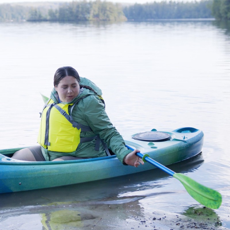 MacKenzie positioning a paddle getting ready to get out of a kayak on the beach.