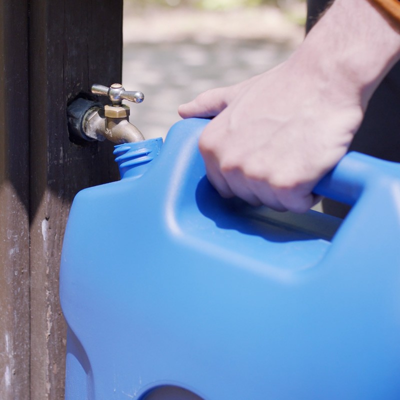 Close-up of a hand filling a large water bucket at a spigot.