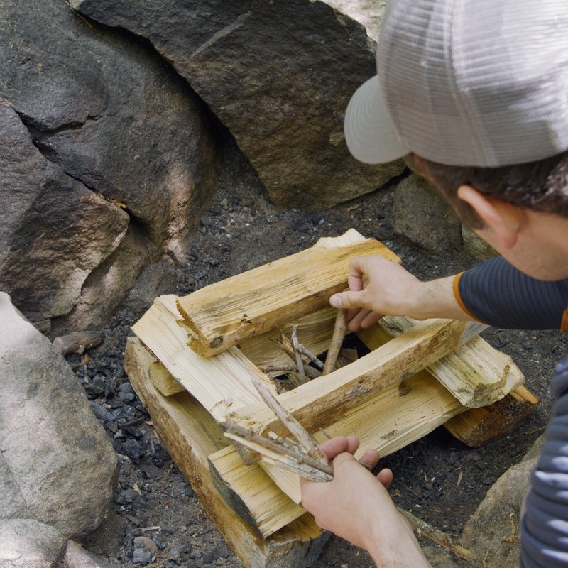 Nate adding tinder to the center of 4 layers of log-cabin style stacked fuel wood.