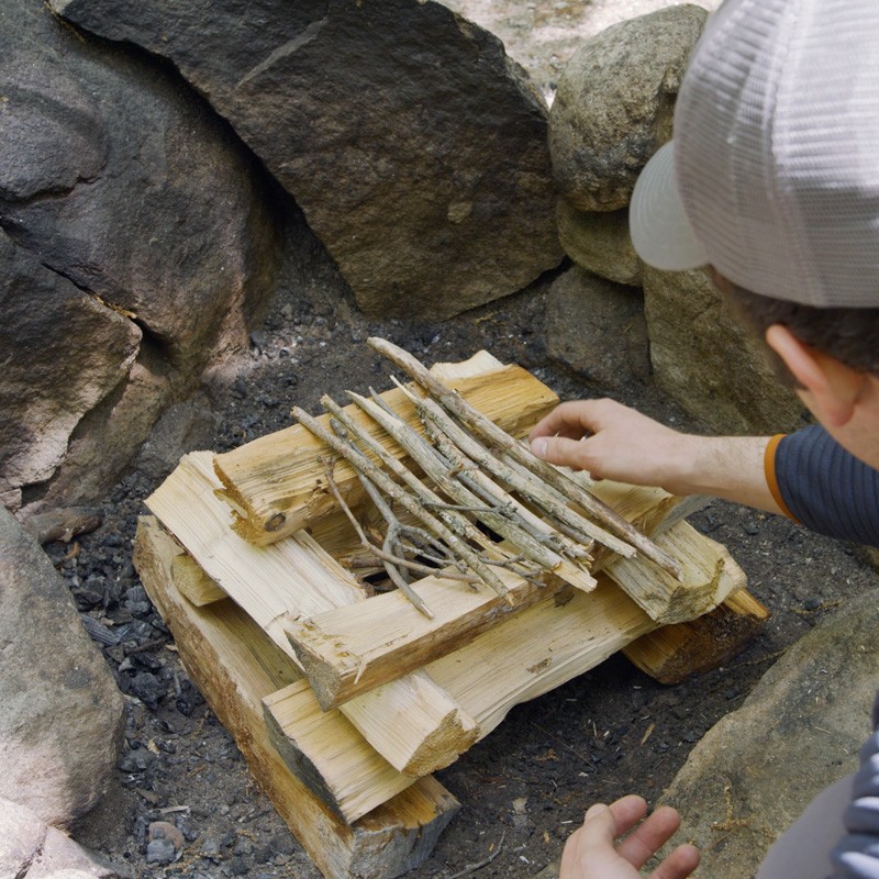 Nate placing twigs across the top of log cabin style stacked wood to form a "roof."