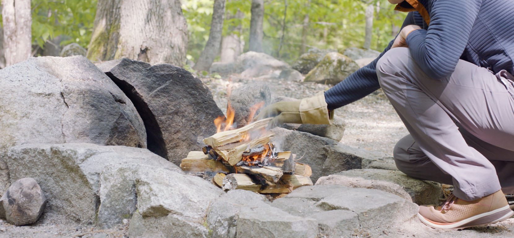 Nate adding wood to the top of a fire wearing a heat resistant glove.