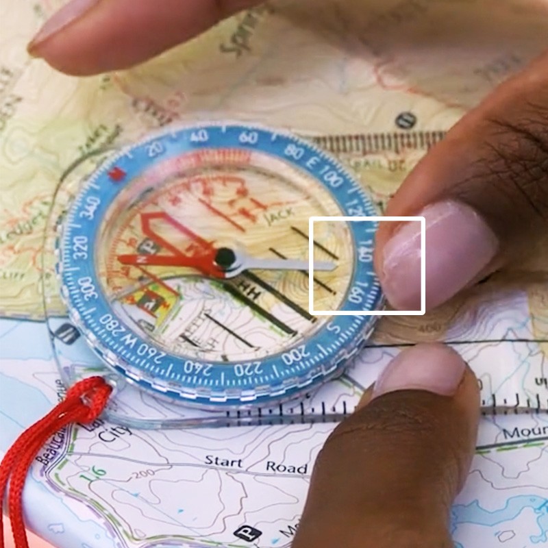 Close-up of a compass on a map with a white square outlining where the magnetic bearing of 159 lines up with the index line.