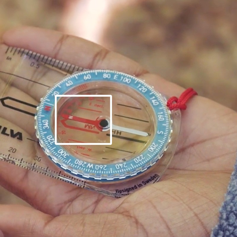Close-up of a compass in Stephanie's hand with a white square around the nesting inside the orienting arrow.