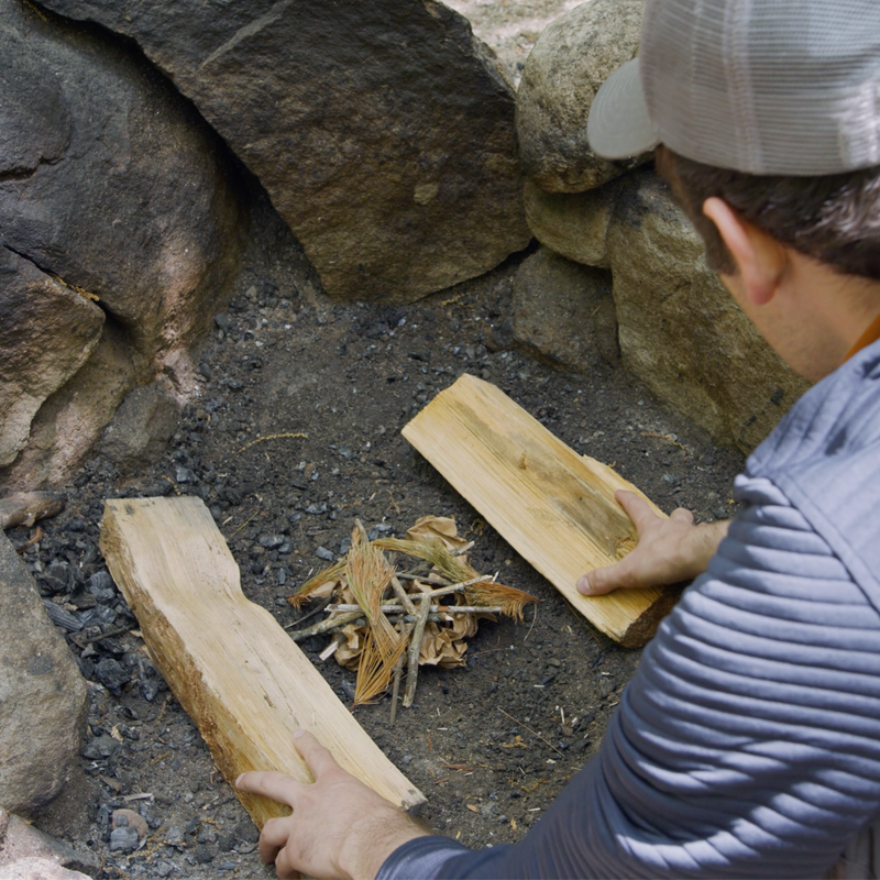 Nate placing a fuel log on either side of a pile of tinder.