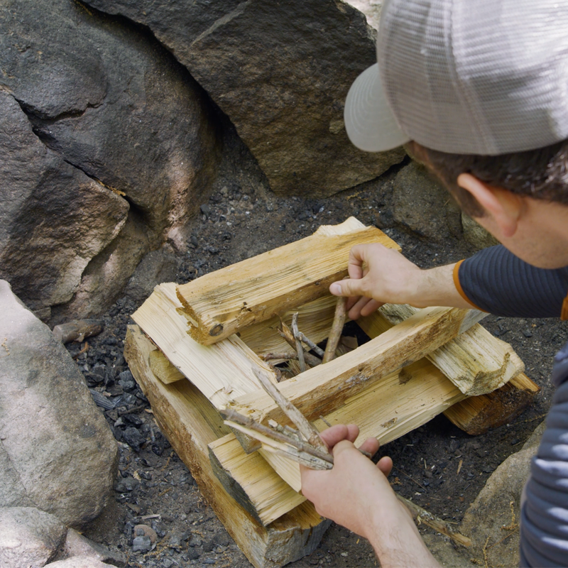 Nate placing small kindling in the center of several layers of log-cabin style stacked fuel logs.