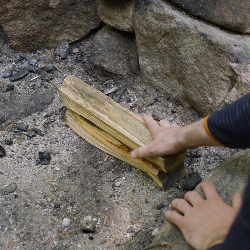 Nate placing a large fuel log toward the back of a fire ring.