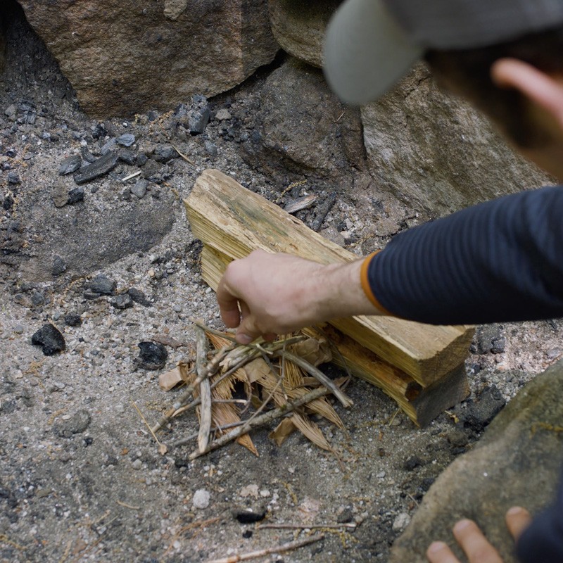 Nate placing a pile of tinder on the leeward side of the log, away from the wind.