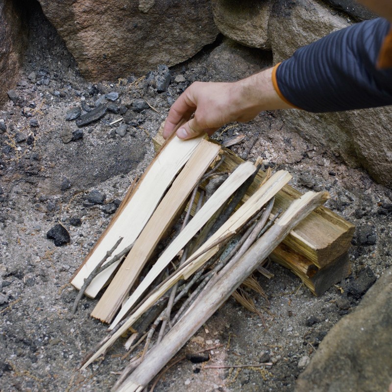 Nate laying kindling against the fuel log and over the tinder like a lean-to.