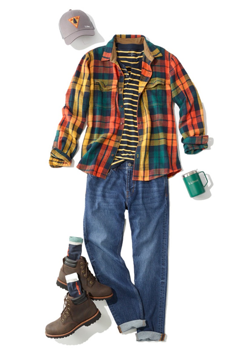 A laydown of an outfit featuring jeans and boots, propped with an insulated mug and a ball cap.