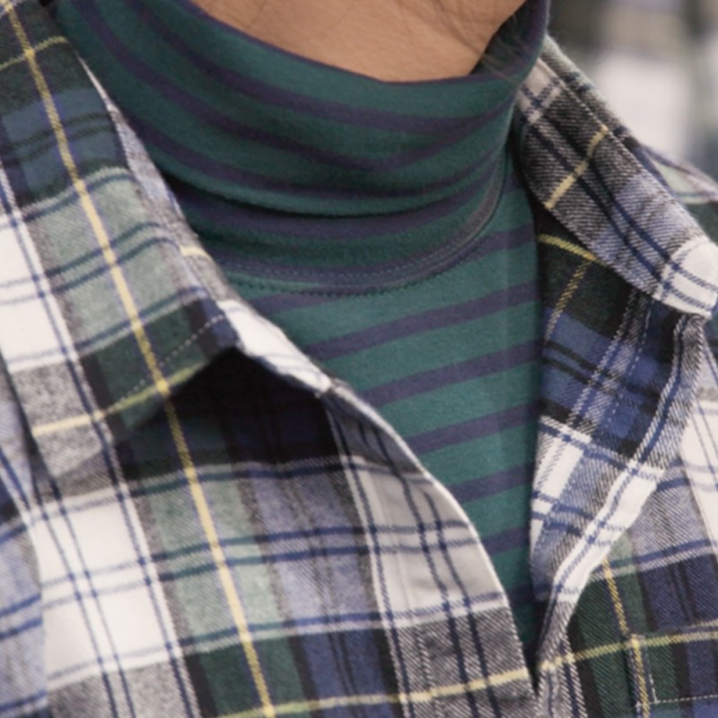 A close-up of a striped turtleneck under a flannel shirt worn by the model.