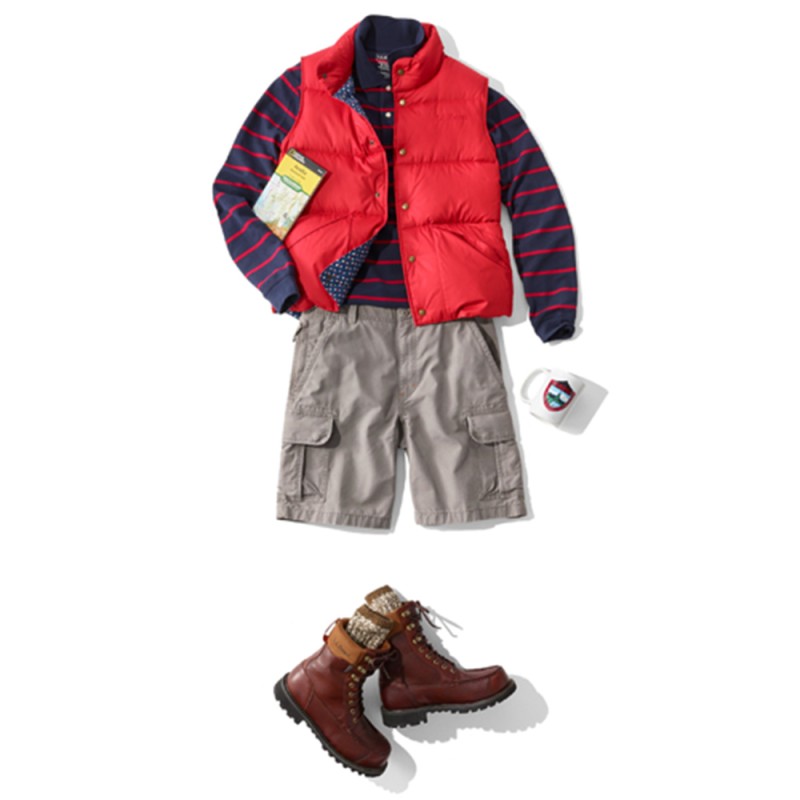 A laydown of an outfit featuring a red puffer vest and shorts, propped with a trail map and a coffee mug.