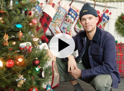 A stylist kneeling next to a festively decorated holiday tree.