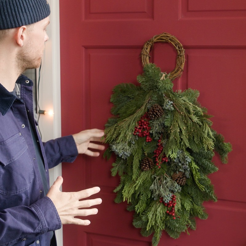 Close-up of Ryan hanging a balsam swag on a red door.