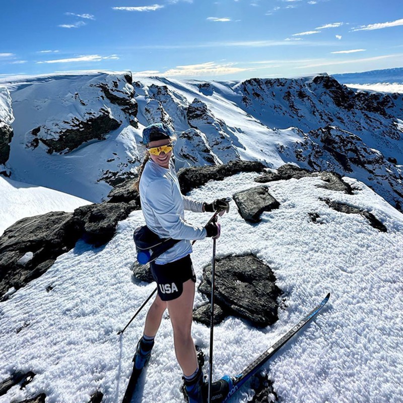 Jessie standing on the top of a snow covered mountain in shorts.