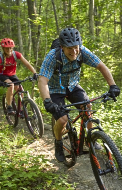 Two pwoplw mountain biking on a wooded trail