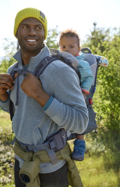 Image of father walking outside wearing a baby carrier holding a younf boy