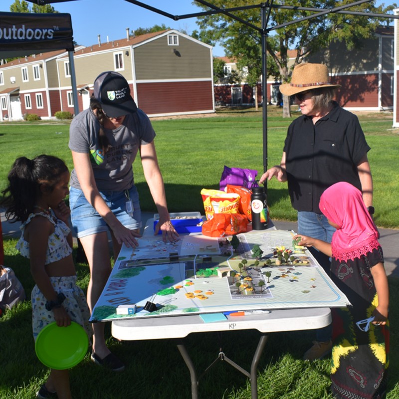 Adults and kids working on a project outside at a table.