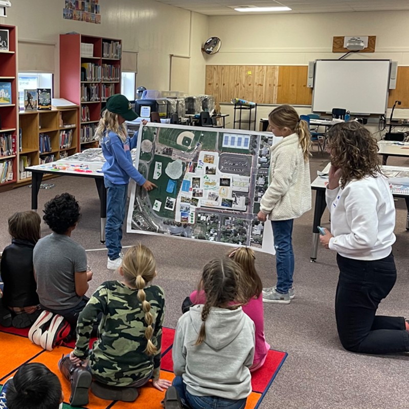2 young students presenting a project to other students and a teacher.