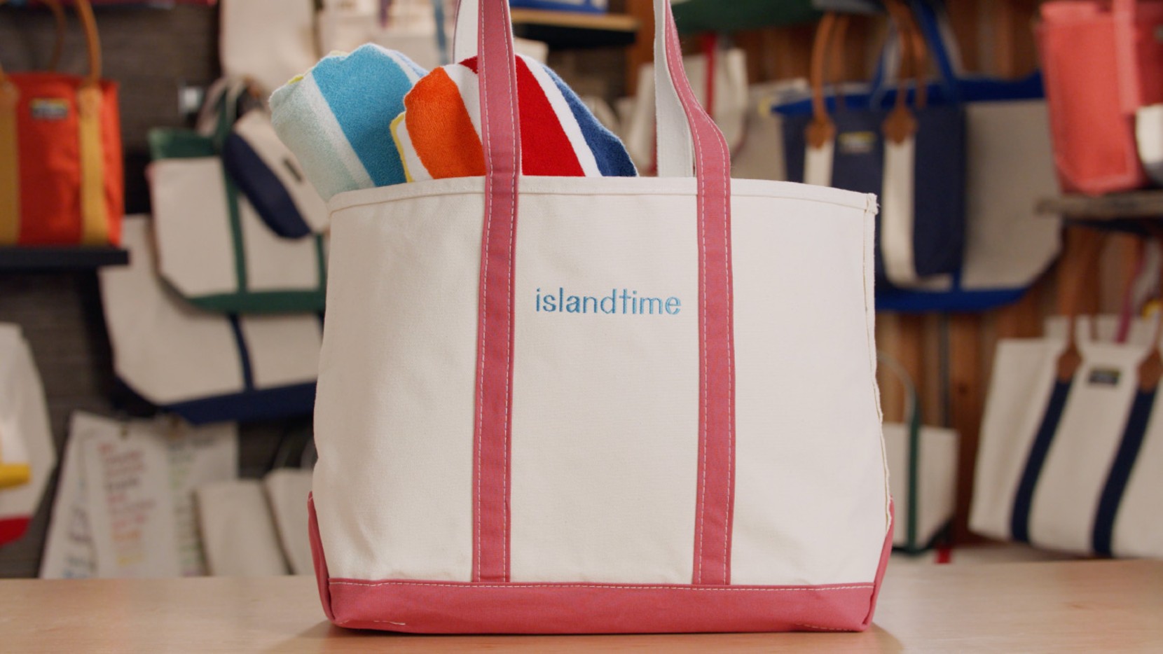 A large Boat & Tote with red handles and light blue monogram - "islandtime", filled with towels and beach toys.