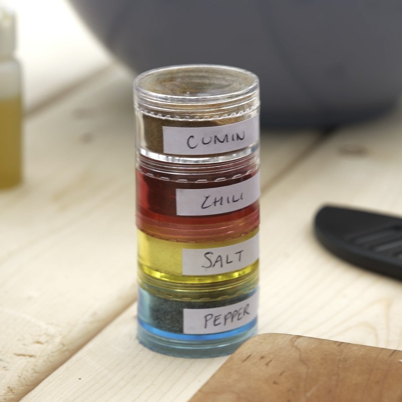Stacked spice containers labeled Cumin, Chili, Salt, and Pepper on a kitchen counter.