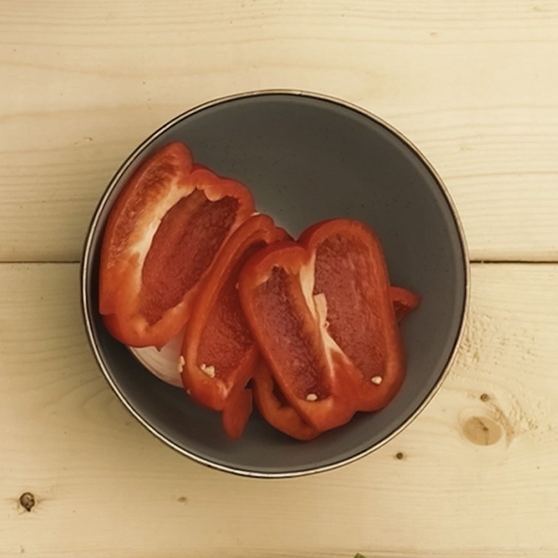 A black bowl containing slices of red bell pepper on a wooden surface.