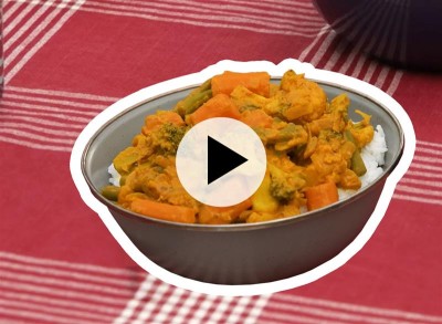 A bowl of curried vegetables sitting on a red and white checkered tablecloth.