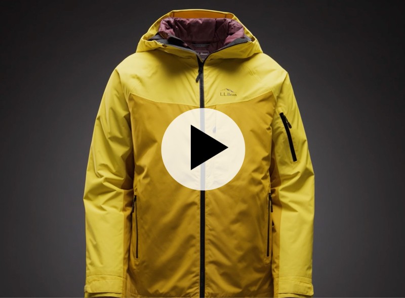 A bright yellow 3 in 1 jacket is on form against a dark gray background with a video play icon in the middle