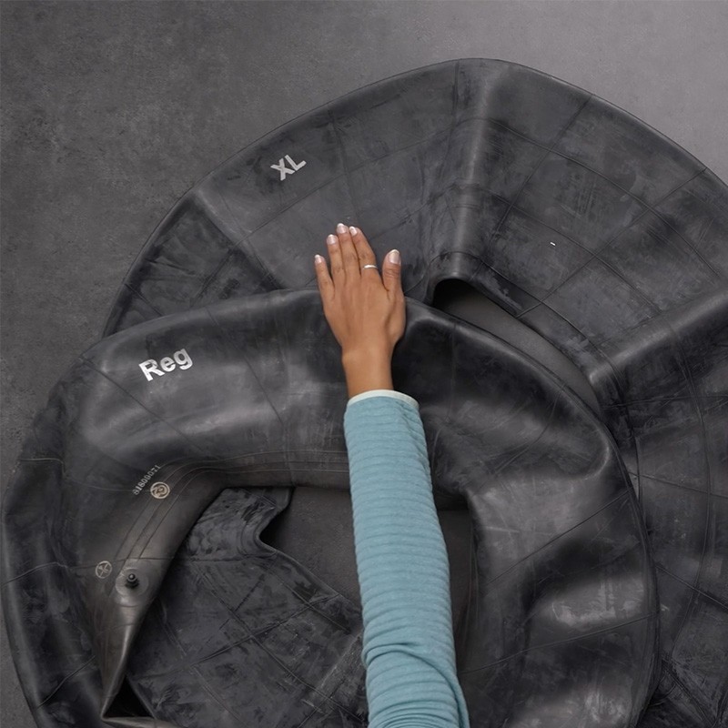 A hand lays out a inner tube flat on a dark gray surface.