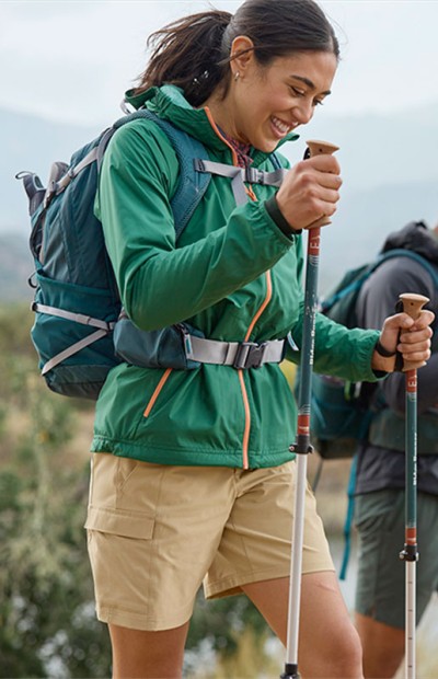 Woman using hiking poles and wearing a hiking pack, outside on a woodland trail.