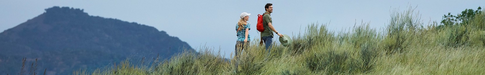 Image of couple hiking in a grassy field with a mountain in the background.