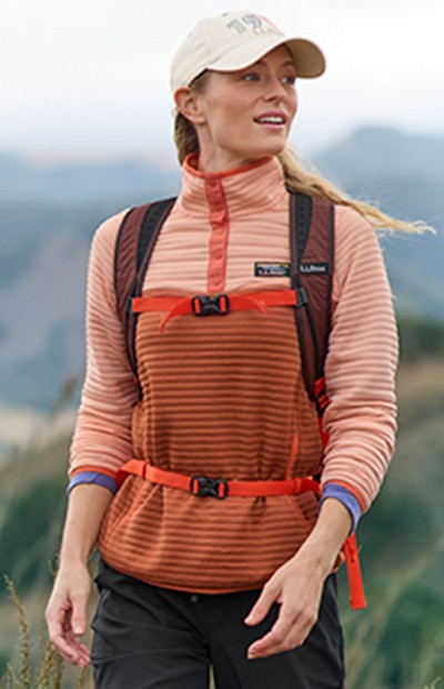 Woman wearing a hiking pack and baseball cap, hiking outside.