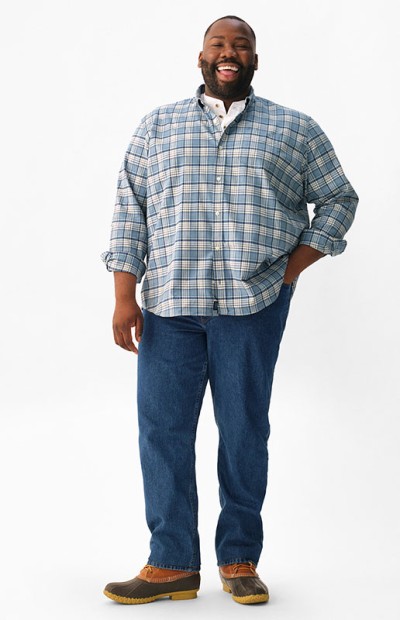 A person stands wearing a plaid shirt, jeans, and brown shoes against a white background.