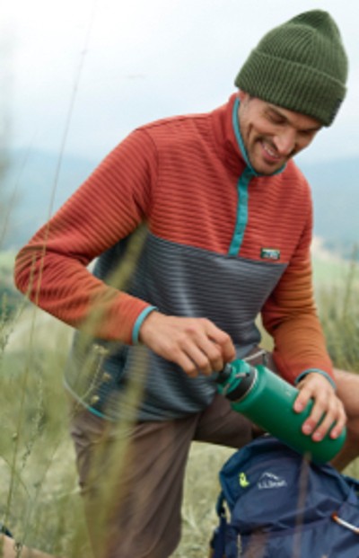 Man using his water bottle while hiking outside on a grassy trail.