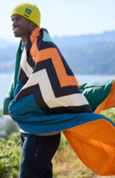 Man wrapped in outdoor blanket with lake and mountain in the background.