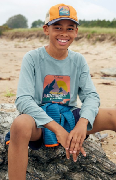Young boy wearing LL Bean ball cap, sitting on a rock at the beach.