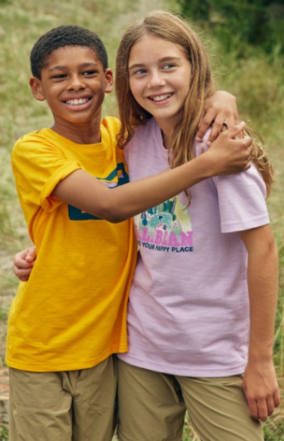 Two young kids smiling and hugging outside with a grassy field in the background.