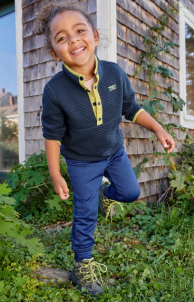 Young child wearing LL Bean clothing walking on the grass outside the home.
