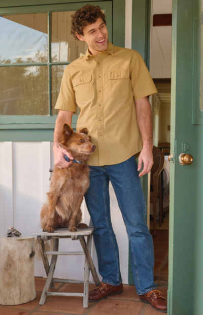 Man standing out front of a house while patting a dog.