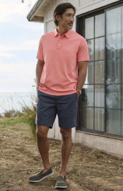 Man wearing LL Bean shorts standing with hands in pockets outside of a house with the ocean in the background.