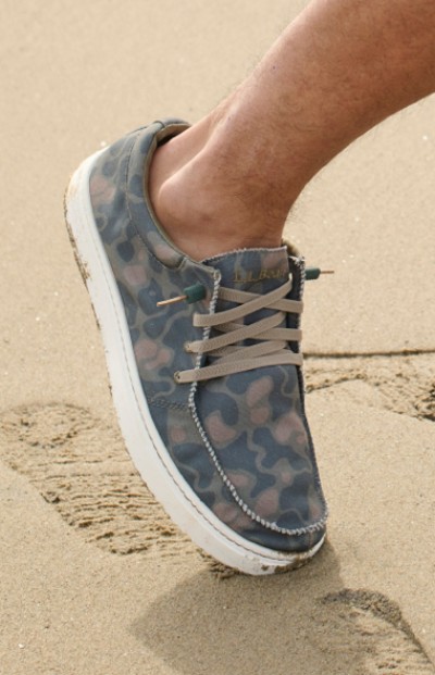 Image depicting a man wearing casual shoes while walking on the beach.