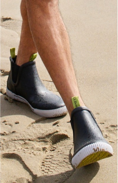Image depicting a man wearing rain boots on the beach.
