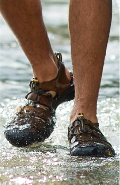 Image depicting a man wearing water shoes while walking in the water.