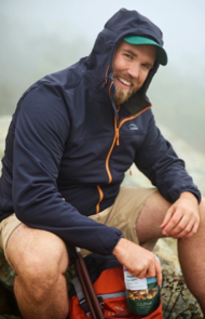 Man wearing fleece jacket sitting on a rock with hikinh gear.