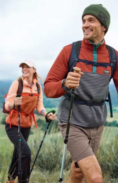 Image of two people hiking with hiking poles on a grassy trail.