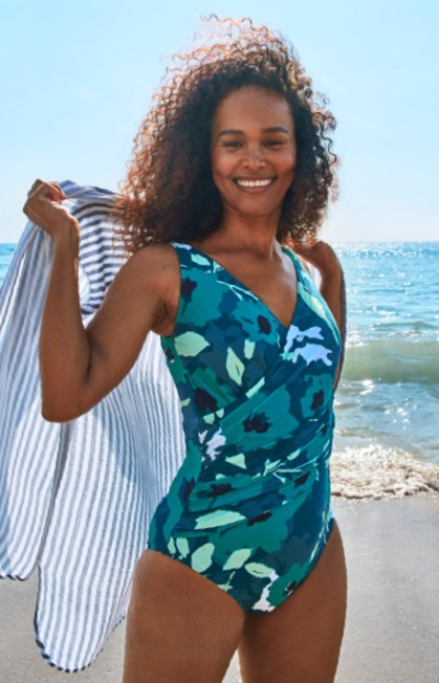 Woman wearing a swimsuit holding a beach towel at the beach.