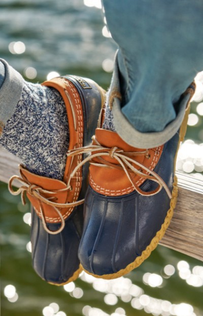 Image of a woman wearing Bean Boots sitting on a fence by the water.